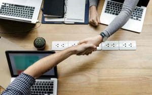handshake over a table with laptops