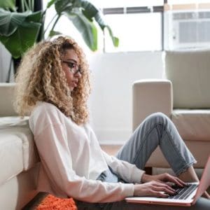 woman working on laptop in apartment with white sofa and plants