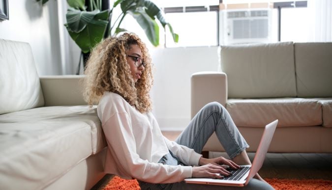 woman leaning against cream sofa in serviced apartment on laptop in daytime