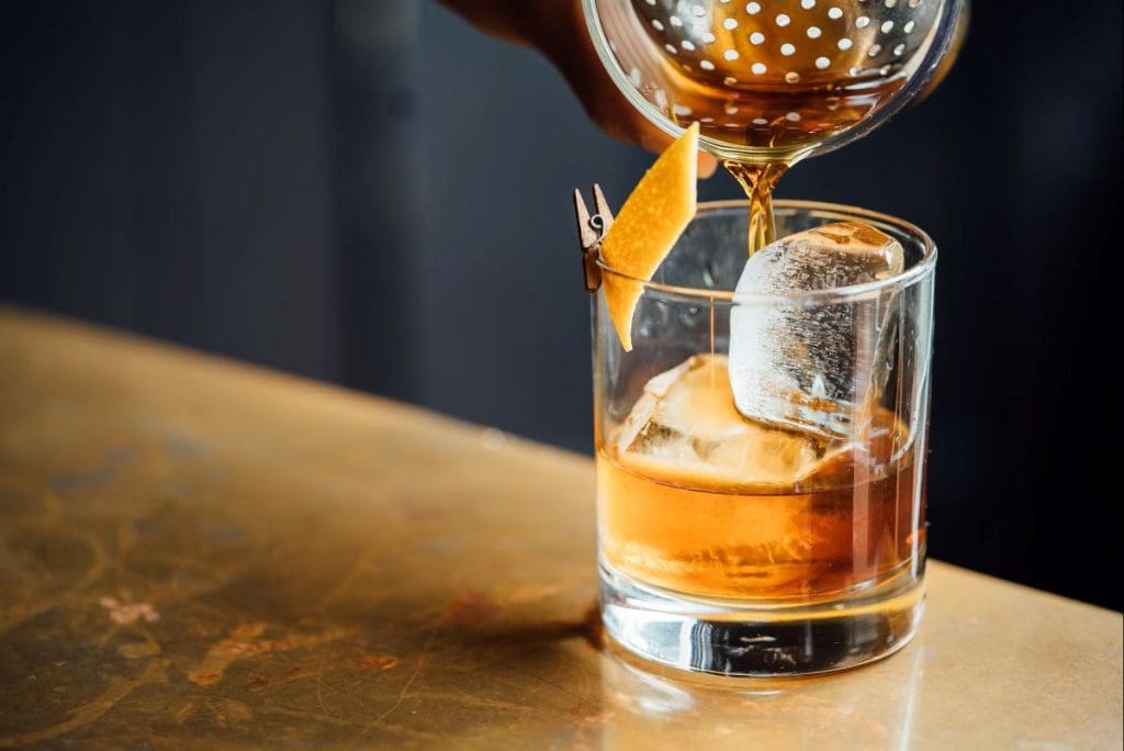 A drink being poured into a glass with ice cubes