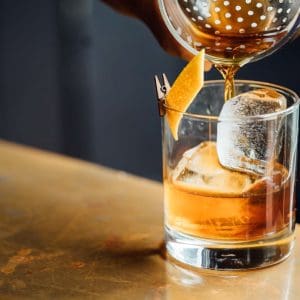 A drink being poured into a glass with ice