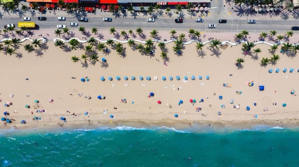 View of a beach in Fort Lauderdale from above, showing palm trees, umbrellas, and people sunbathing