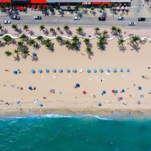 View of a beach in Fort Lauderdale from above, showing palm trees, umbrellas, and people sunbathing