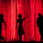 Three people standing behind a red curtain on a stage